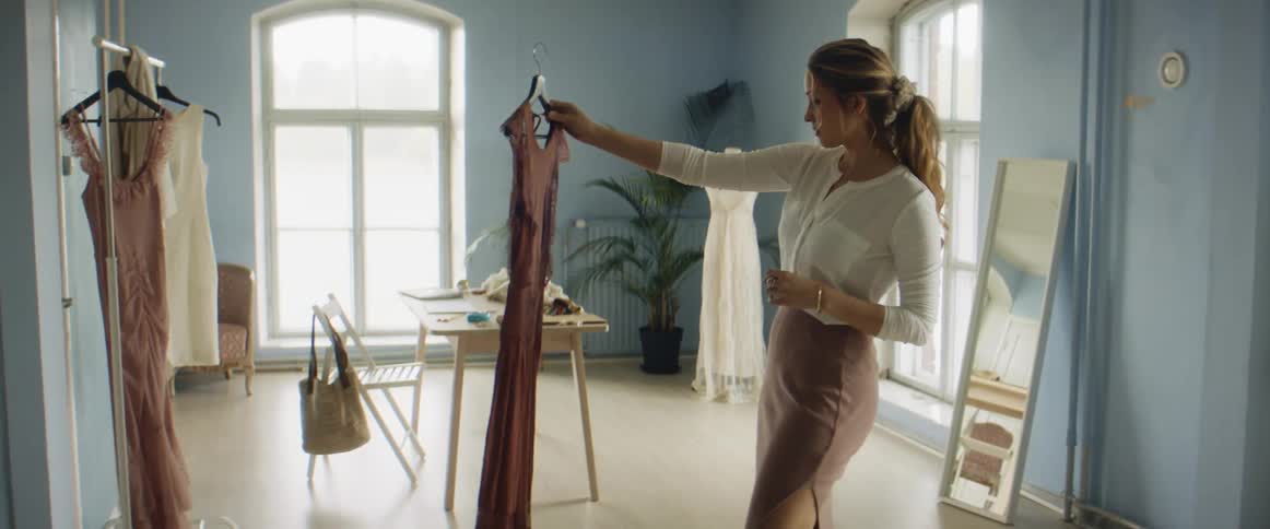 A woman in a shop examines a dress and then hangs it up