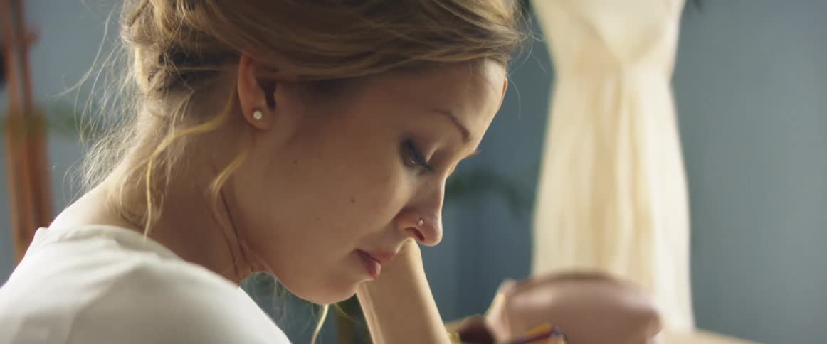 A woman sits in a room with a wedding dress behind her