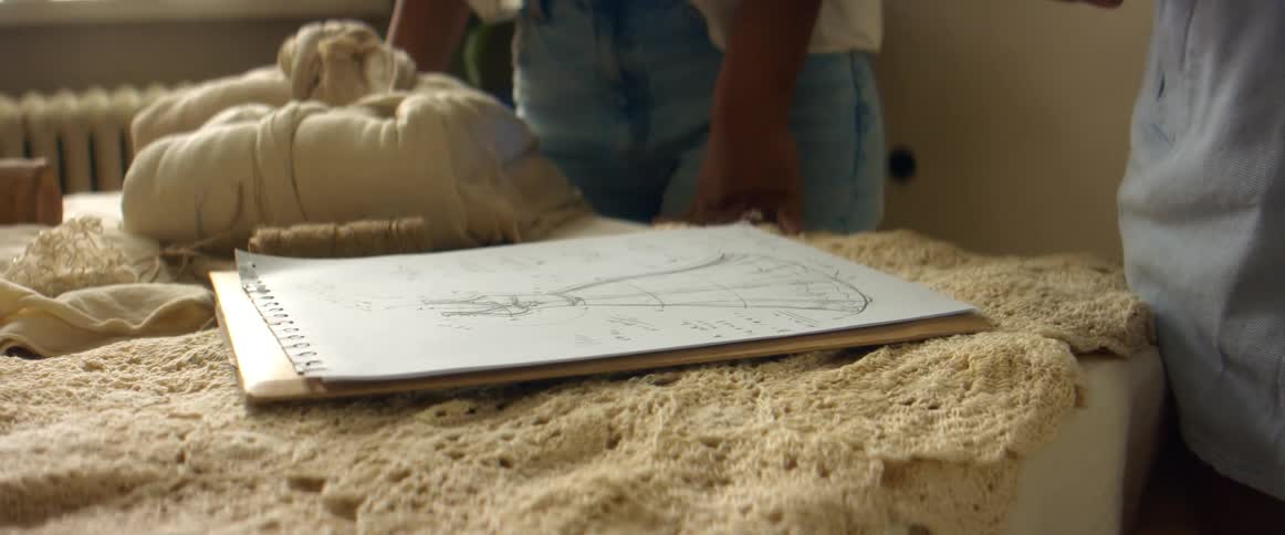 A man and woman discuss a design sketch as they stand behind a table with mounds of clay