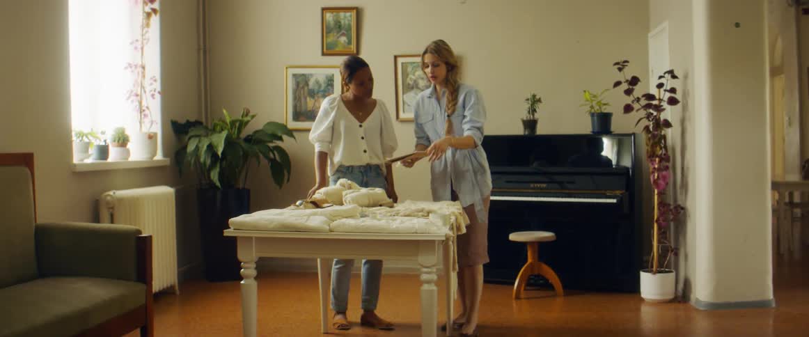 Two women in a house look at notebook and clothing on a table