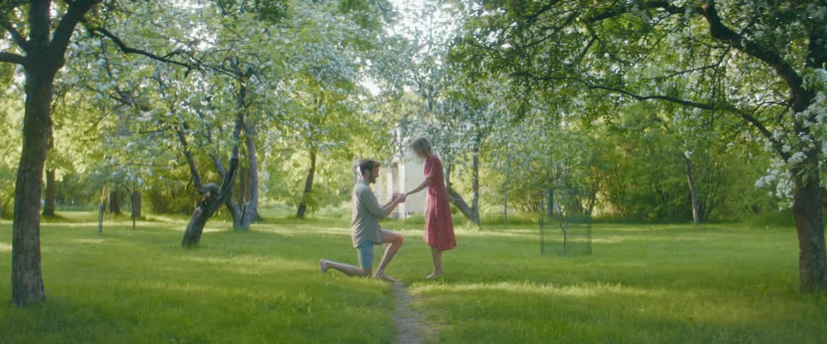 A man kneels on one knee to propose to a woman standing in front of him