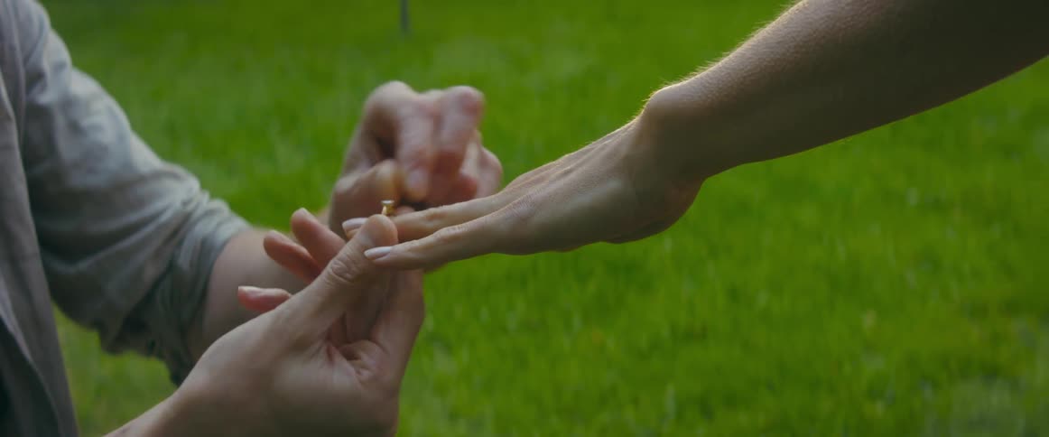 A kneeling man places a ring on the finger of a woman before standing and embracing her