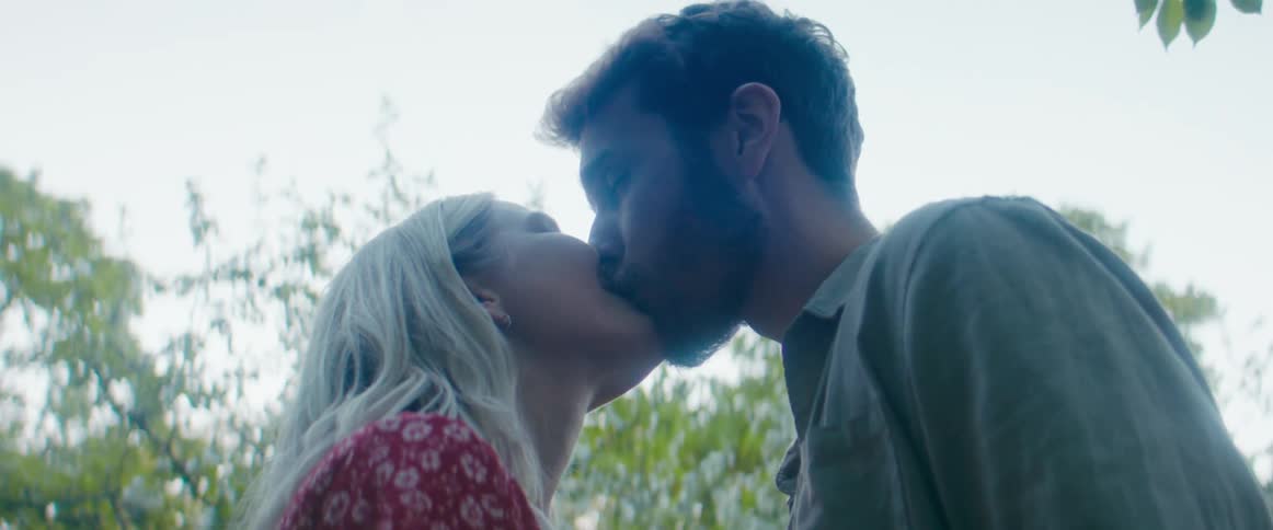 A couple kiss outside on a cloudy day