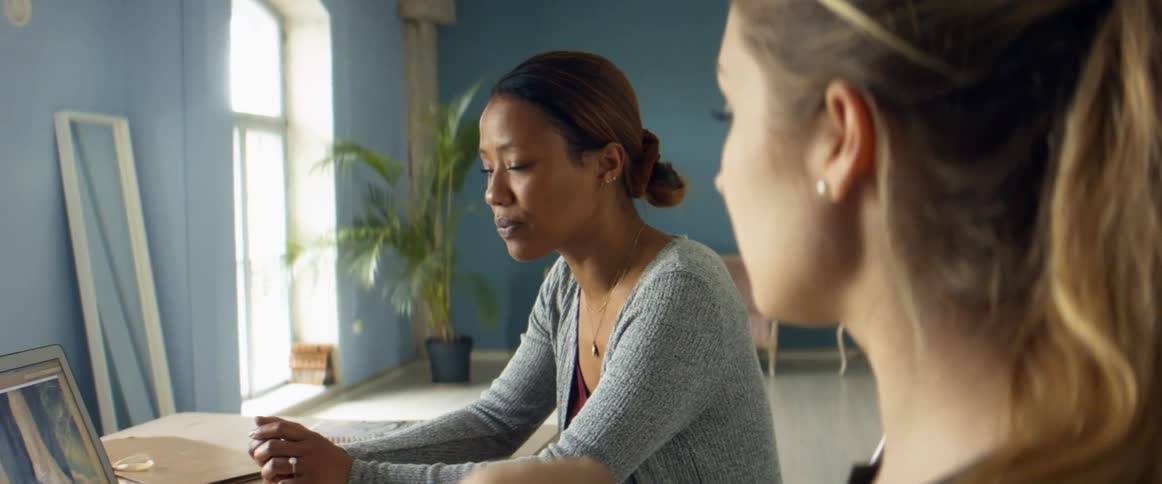 Two women in a shop look at a fashion design on a laptop