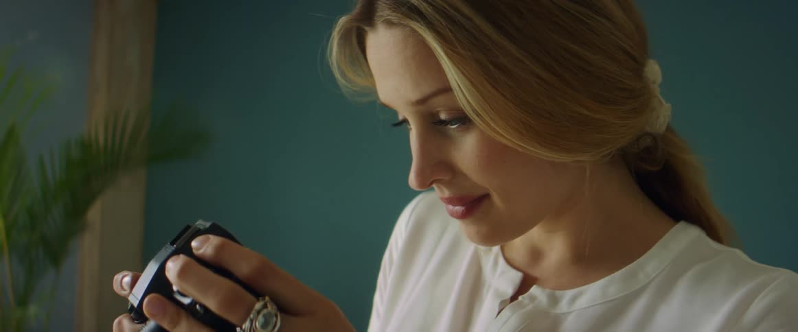 A woman in a room looking at a camera with a wall and plant in the background