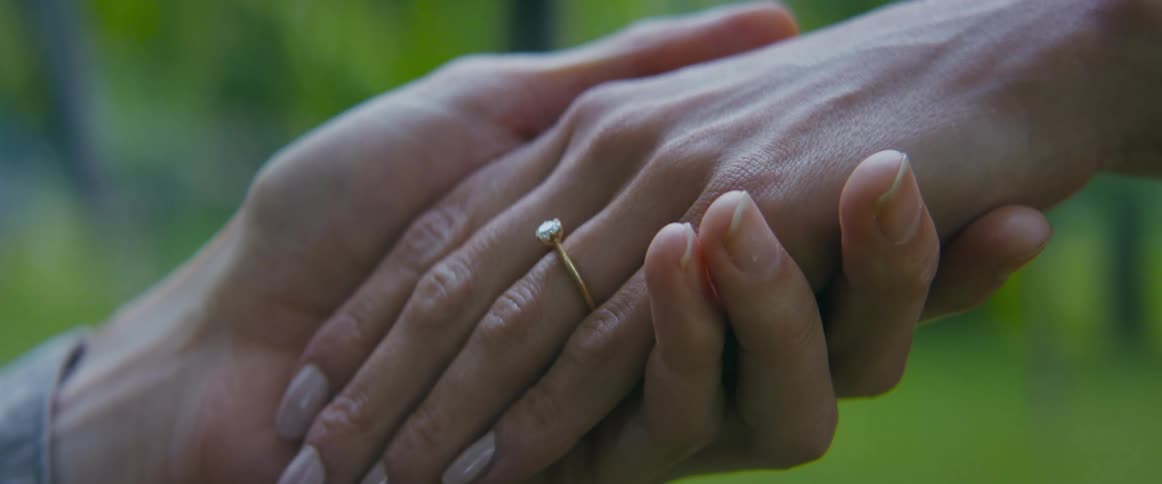Man holding a womans hand with an engagement ring on one finger