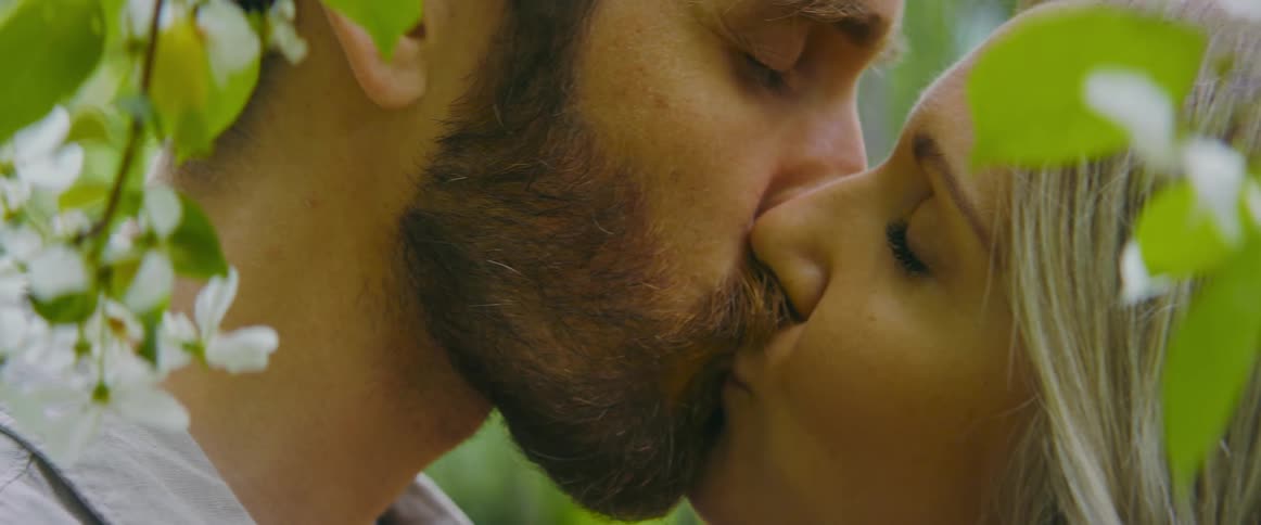 A man and a woman kissing with leaves and flowers in the foreground