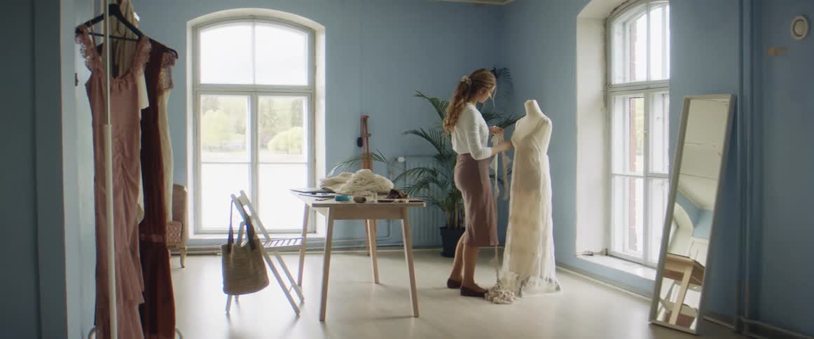Clothing designer works with gown on mannequin in studio