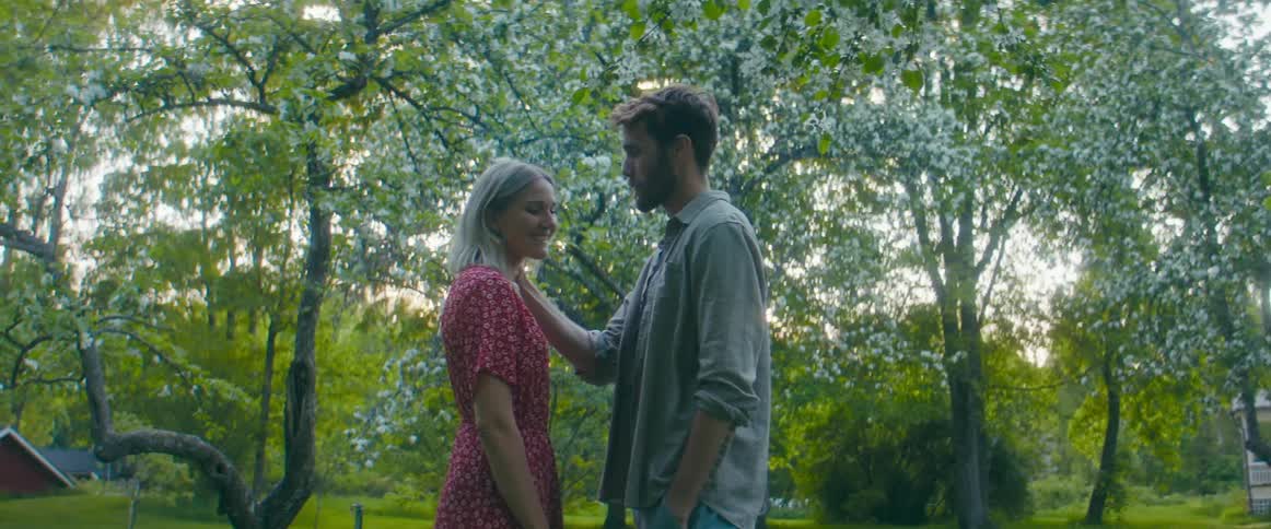 Man puts a flower in a womans ear before kissing at sunset