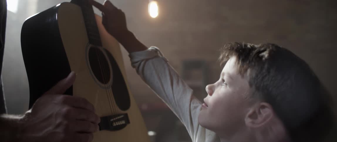 A boy touches a guitar his father is holding
