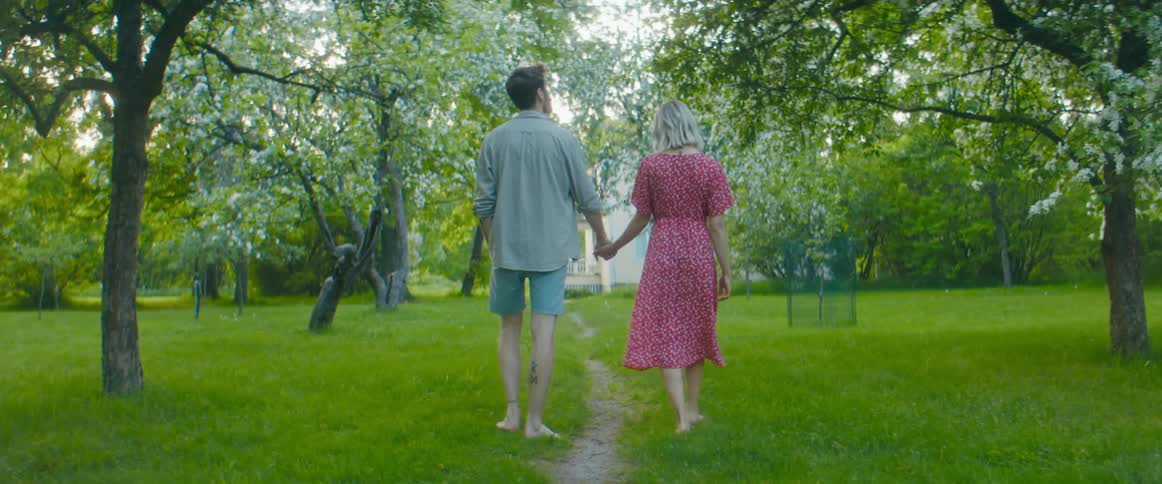 A man and woman hold hands as they walk through a park