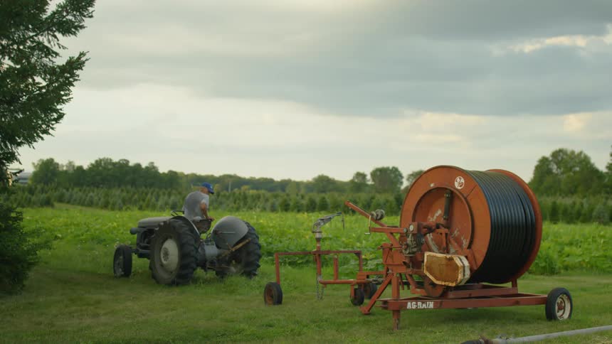 A man is on a tractor by his farm at dusk