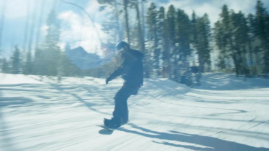 A person with a helmet and goggles snowboarding down a slope with trees the sky and clouds in the background