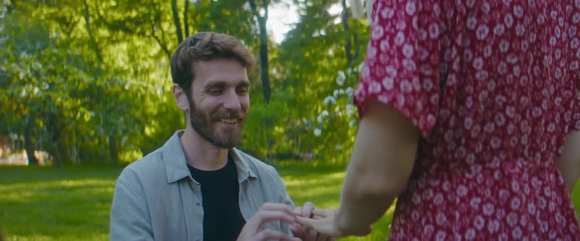 Man smiles as he kneels to propose with ring before he and future wife hug