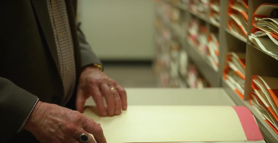 A man chooses a manilla envelope from a shelf full of envelopes and opens it on a small table
