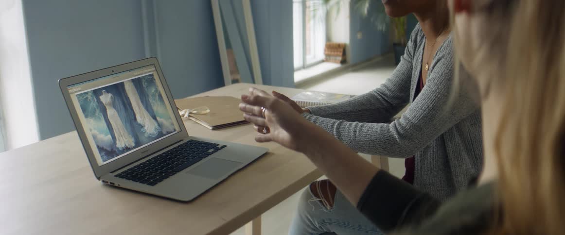 Two women in an office look at a dress on a computer and discuss it
