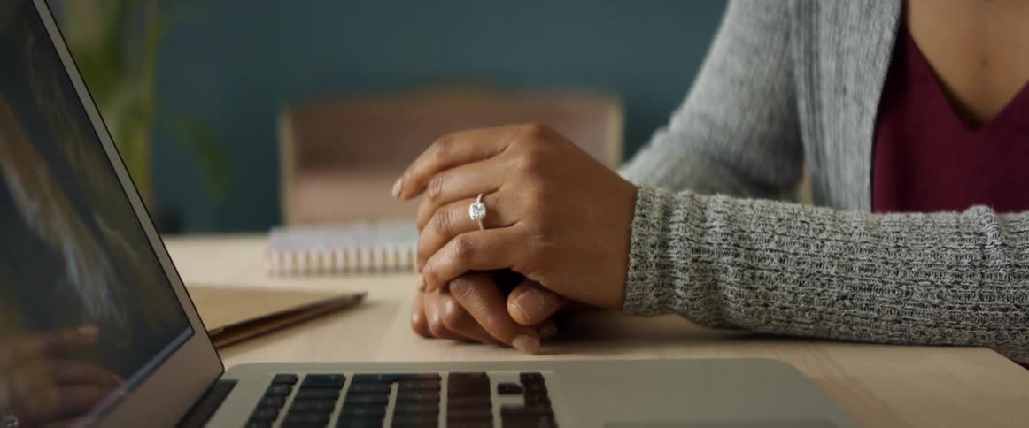 An engaged woman sits with her hands crossed while looking at a laptop