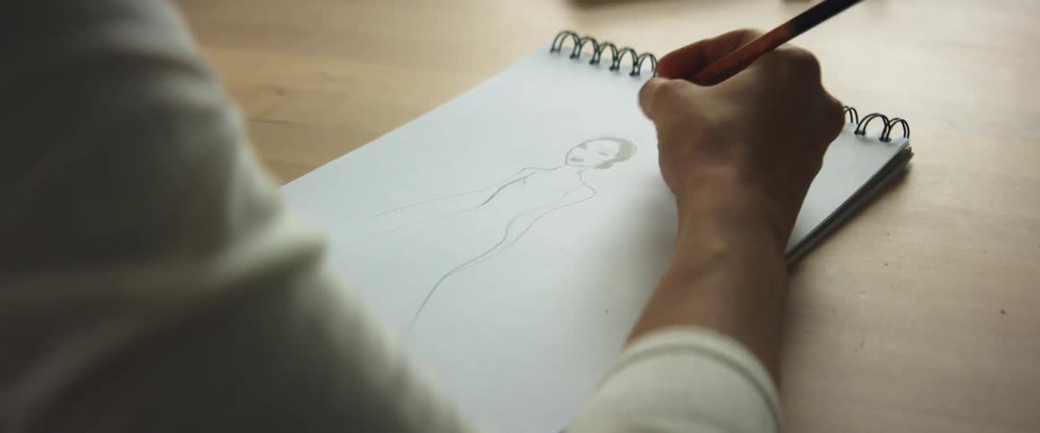 Person sketches on drawing pad set on wooden surface