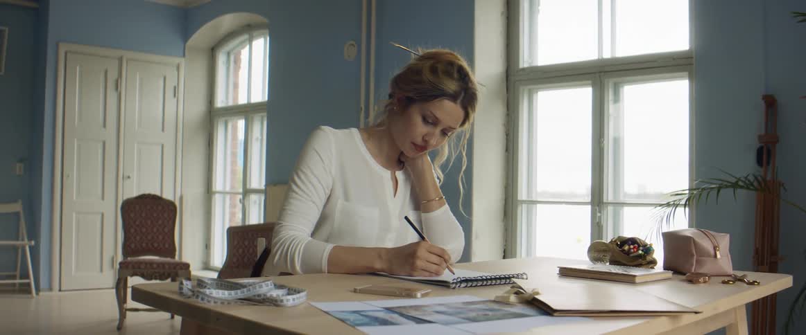 Young blonde fashion designer drawing a design on paper on her studio