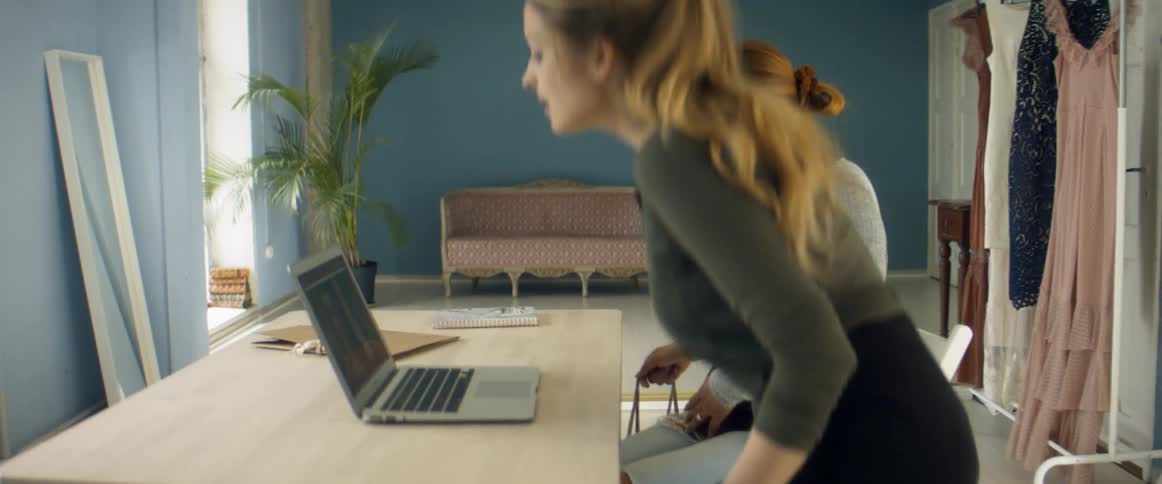 Clothes designer talking to a client in her studio sitting on a desk in front of a laptop