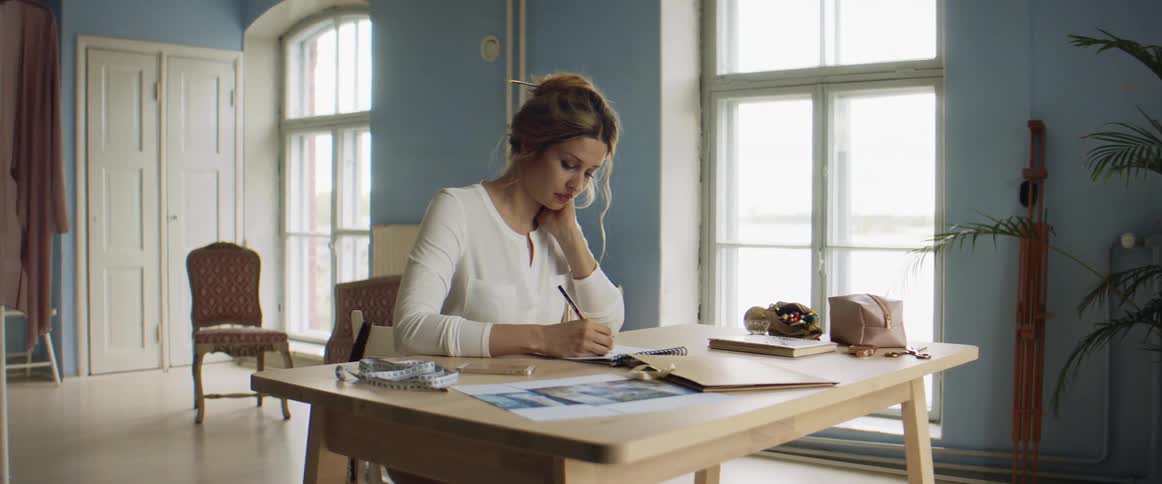 Young blonde fashion designer drawing a design on paper over a desk on her studio
