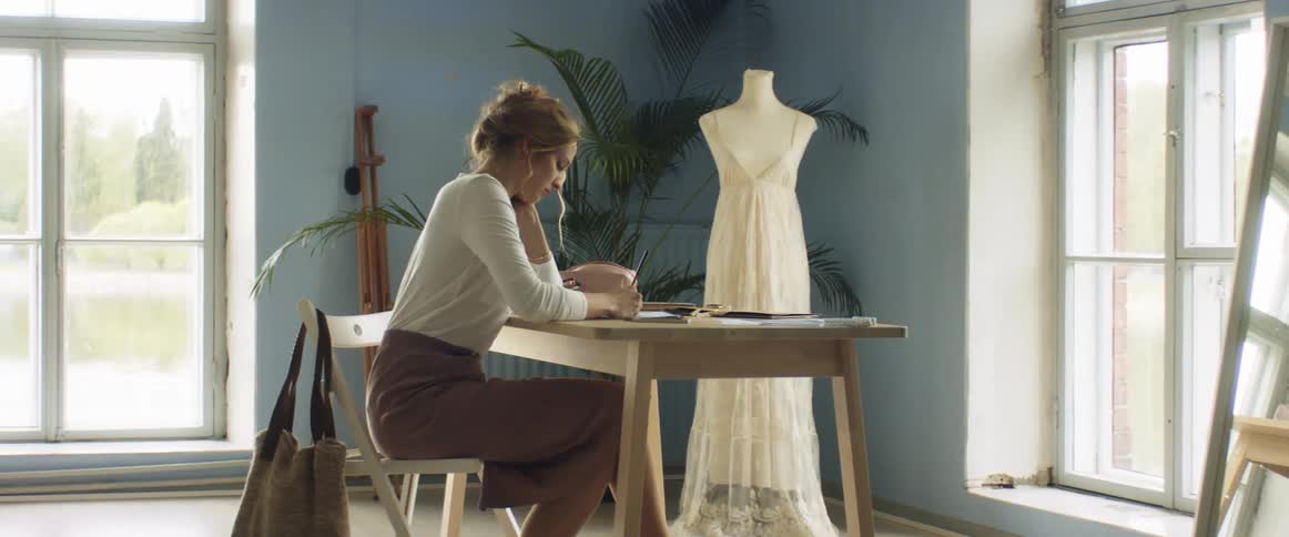 A woman sits at a desk in a shop and sketches