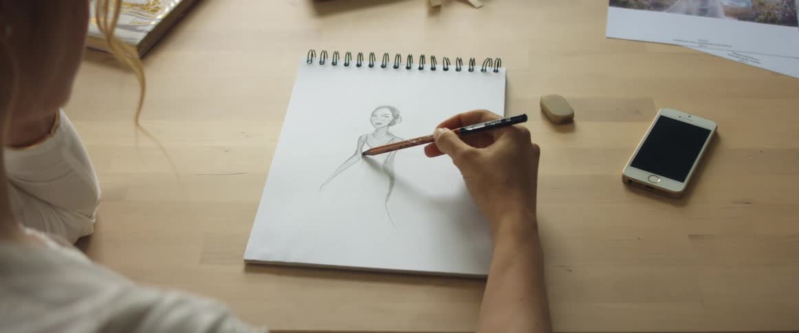A woman sketches a wedding gown in a notebook
