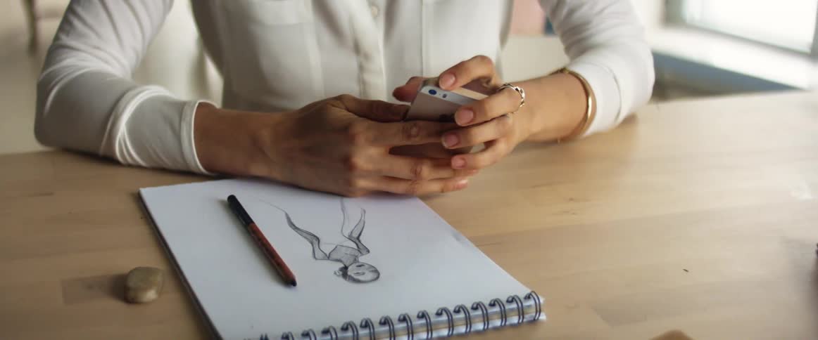 A woman sitting at a table with a pencil and pad using a smart phone