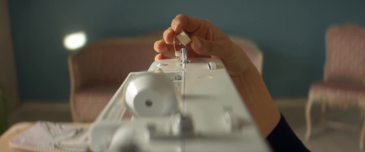 A person removes a spool of thread from the top of a sewing machine