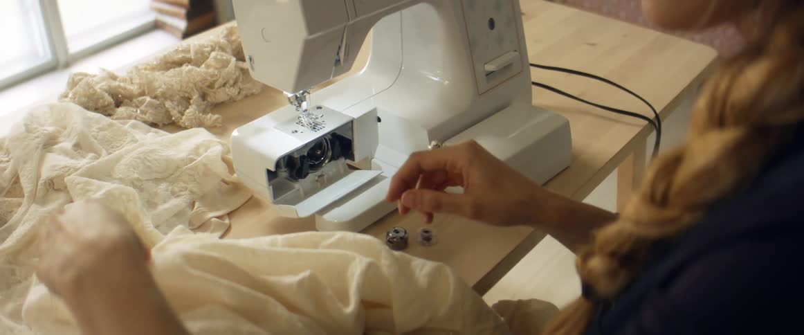 Young blonde woman threading a sewing machine inside a room