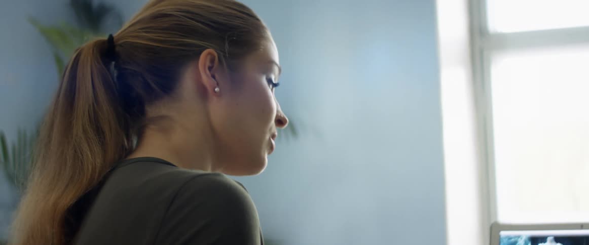 A woman in a room with a plant a wall and a window in the background