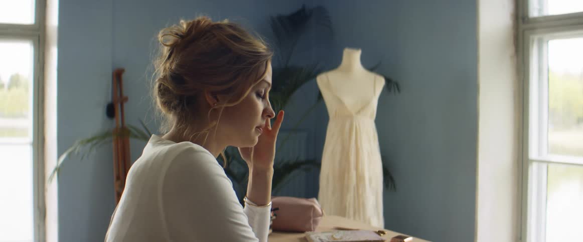 A woman sits down at a table in her design studio rubbing her forehead