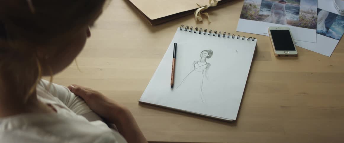 Young blonde fashion designer looking at a design on paper over the desk on her studio