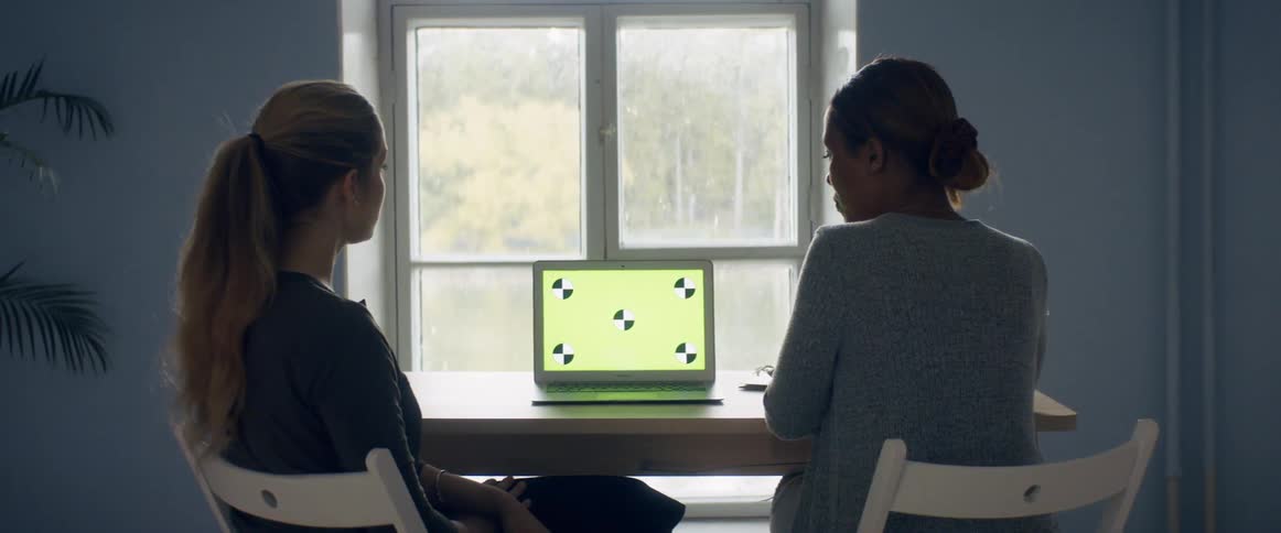 Two women are talking together and sitting by a laptop
