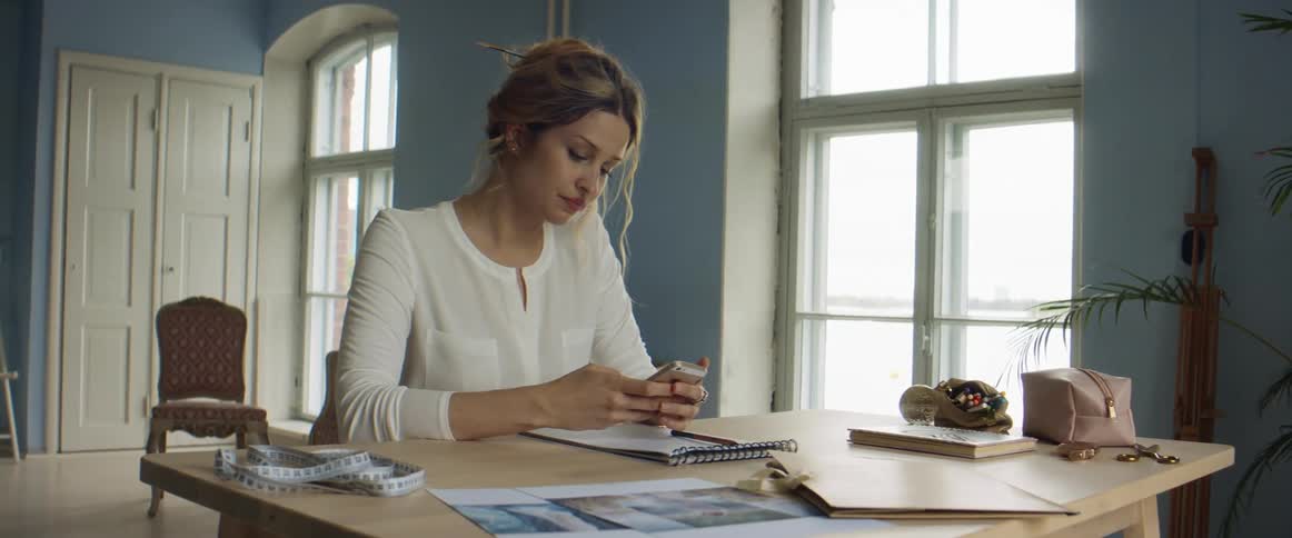 A woman picks up her phone and starts typing as she is sitting at her desk