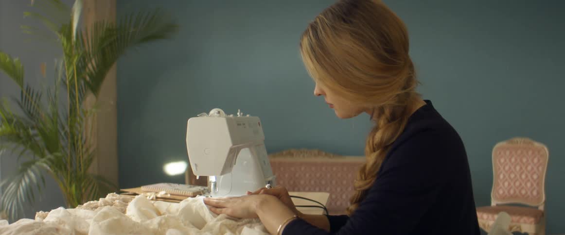 A woman carefully uses her sewing machine while making a dress