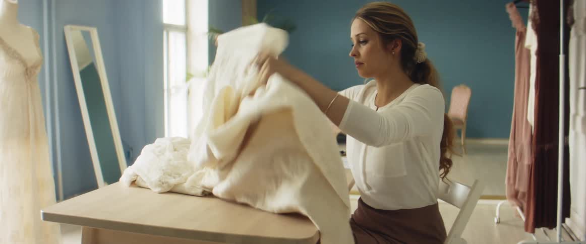 A woman sits at a table and looks at difference pieces of fabrics in front of her