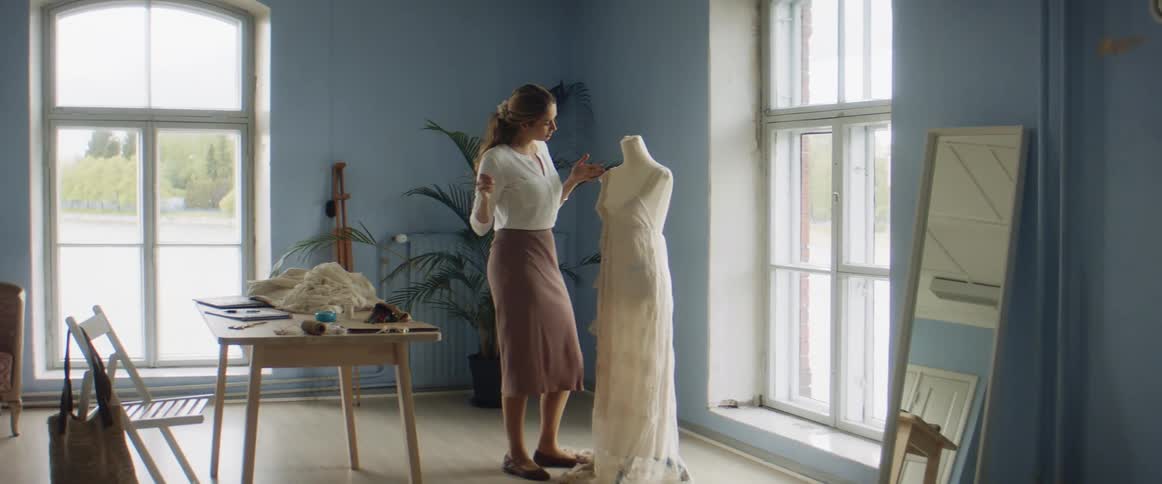 A seamstress works on a dress on a dress form in a bridal store