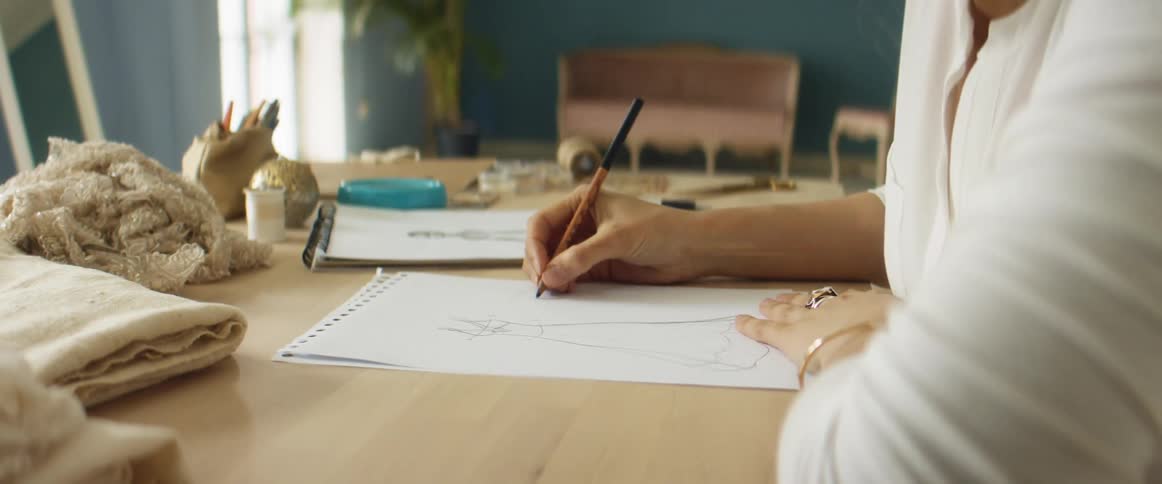 Young blonde fashion designer drawing a design on paper over a desk on her studio