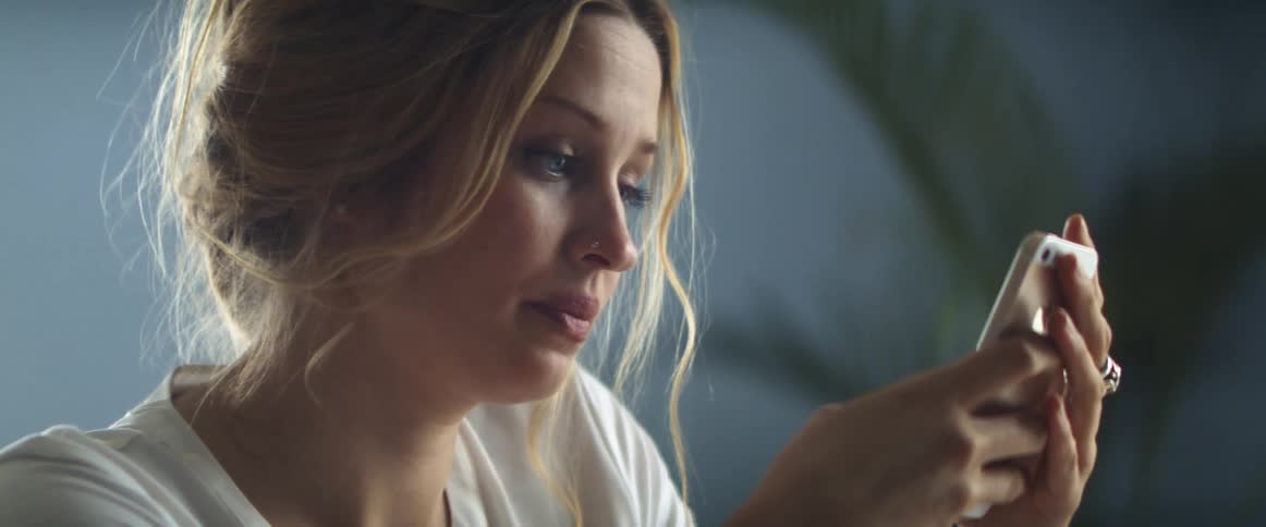 A woman in a room using a smart phone with a wall and a plant in the background