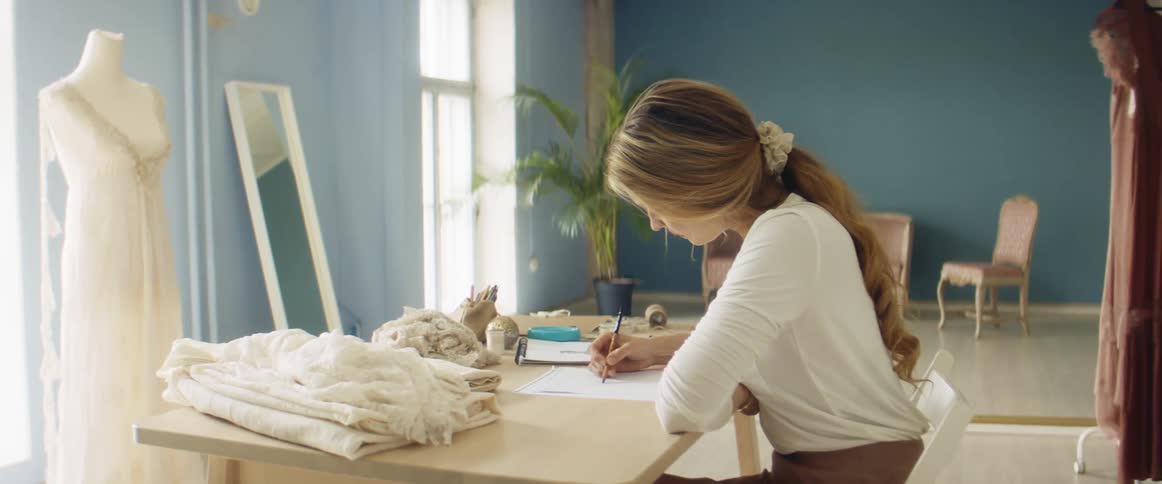 A woman is sitting at a desk and working on a pencil sketch