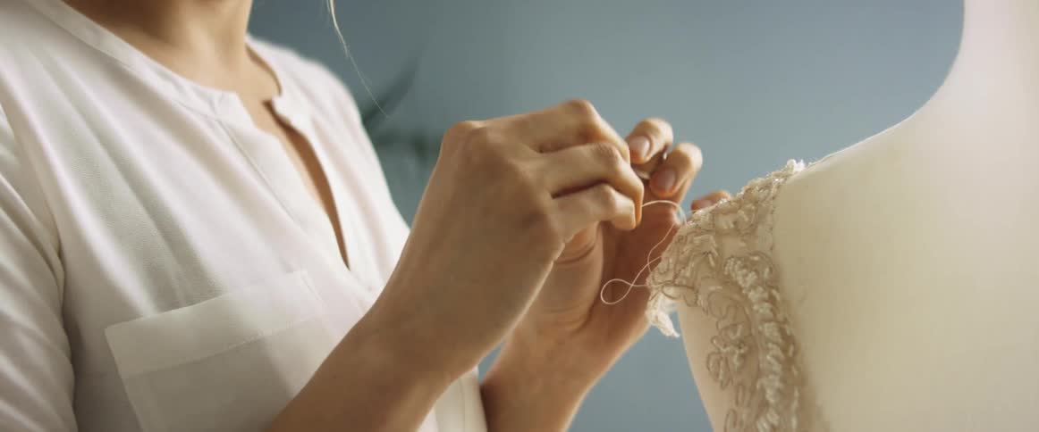 Woman sews shoulder of sleeveless intricate top set on dummy