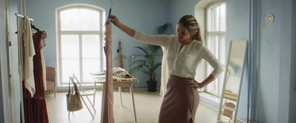 A woman holds up and looks at a dress in a clothing store before putting it on a rack