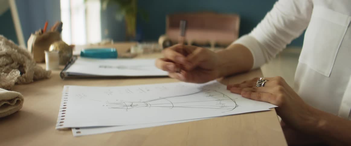 Young blonde fashion designer drawing a design on paper over a desk on her studio