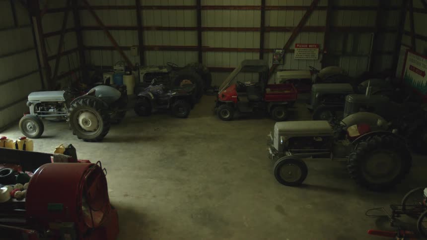 Opening vehicle barn brightens dim area with multiple parked agriculture vehicles
