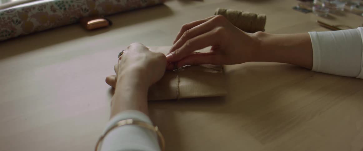 A woman ties a bow with twine on a package wrapped in brown paper