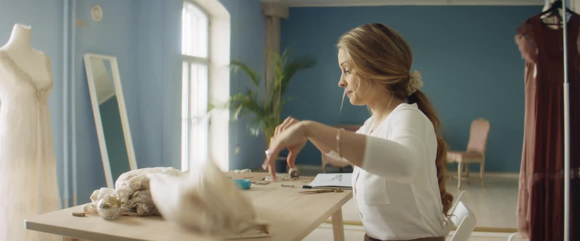 A woman sits at a table where she folds a large piece of fabric