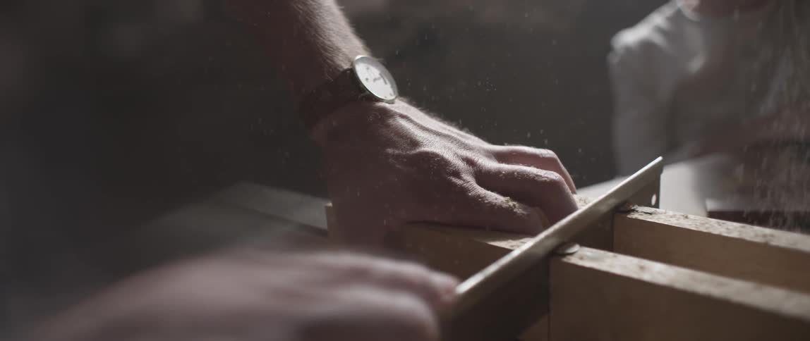 A hand holds a piece of wood in one hand and saws it with the other