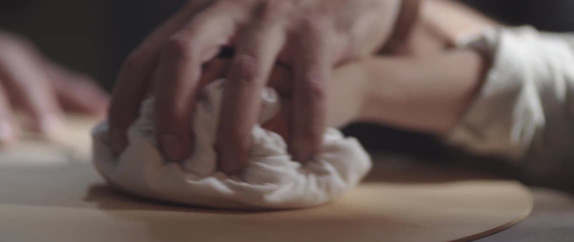Two peoples hands place on a cloth to polish a piece of wood