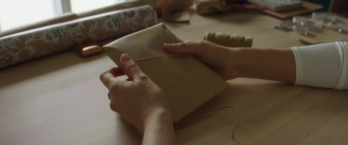 A person is folding an envelope while sitting indoors